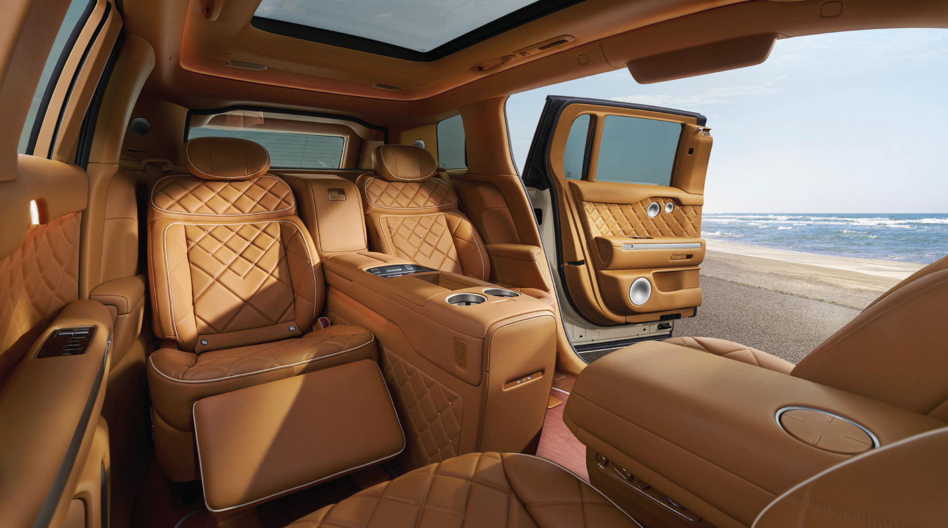 Luxurious car interior with tan quilted leather seats and an open door revealing a sunny beach and ocean.