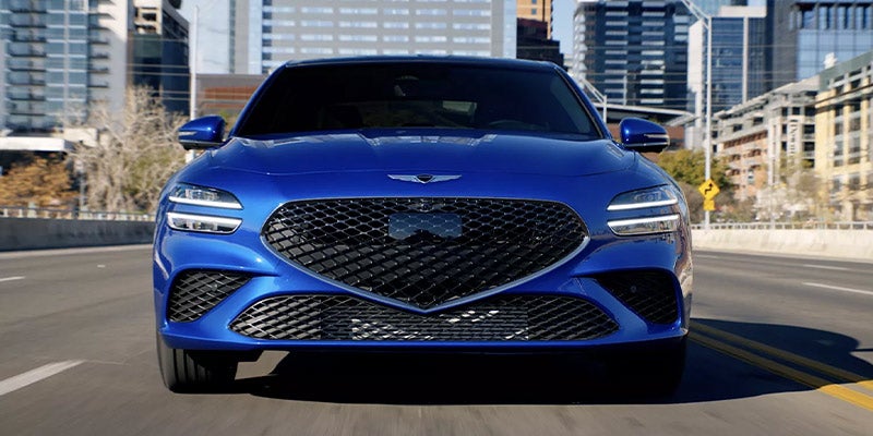 Front view of a blue luxury sedan driving on a city street.