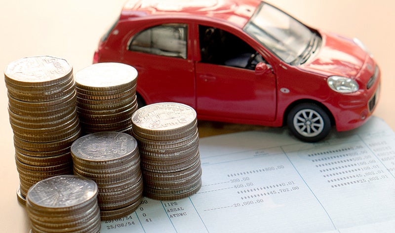 Stacks of coins placed beside a red model car on top of financial documents, illustrating vehicle financing, savings, or ownership costs