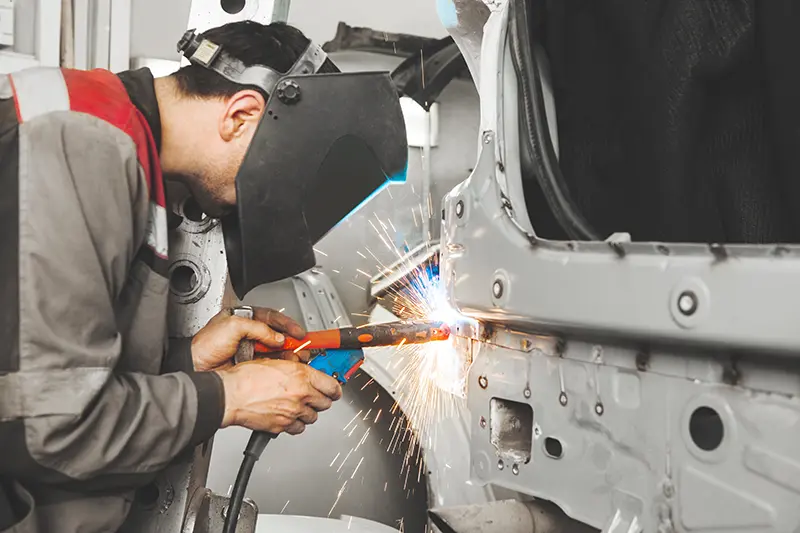 Technician performing body repair and welding work on a Genesis vehicle.