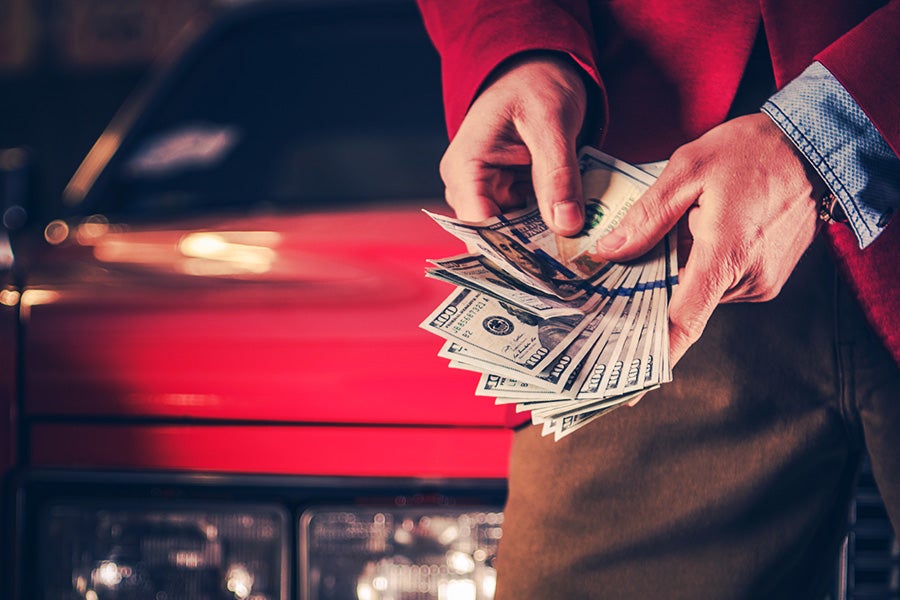 A close-up scene showing a person handling a large amount of cash in front of a vehicle